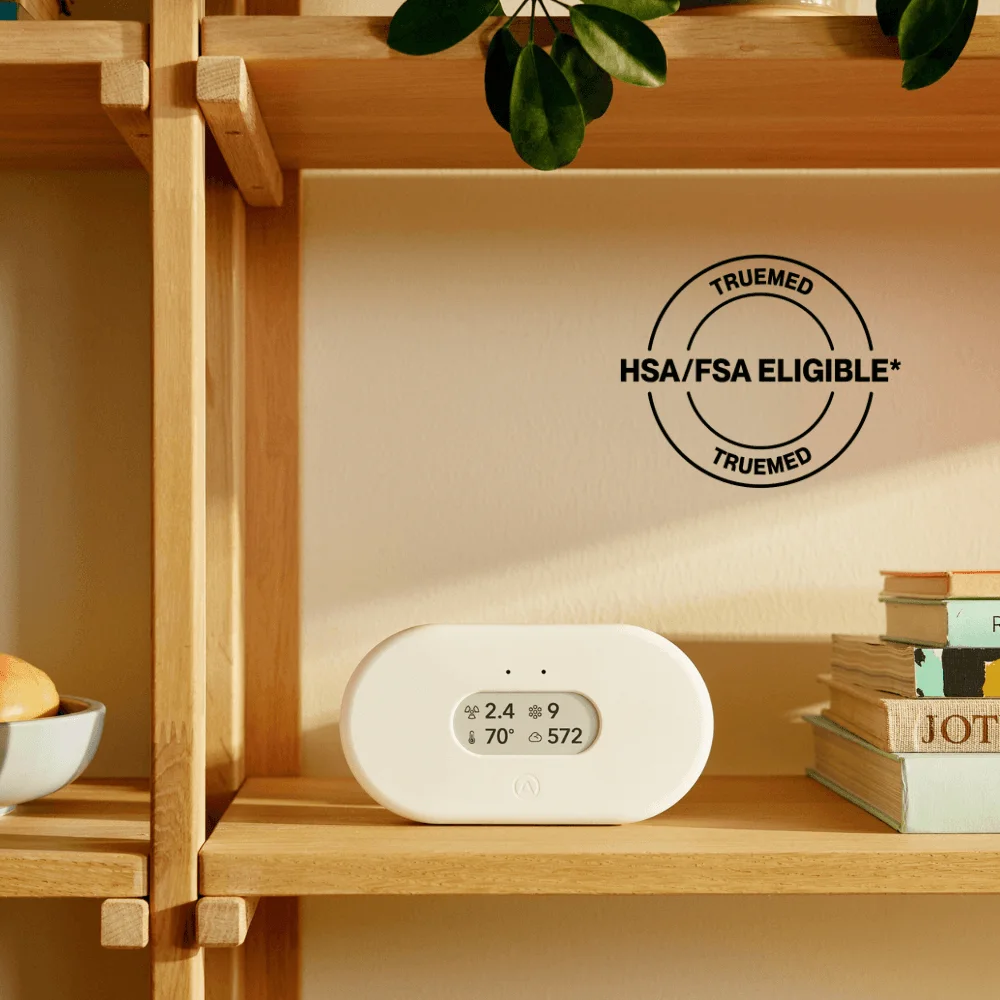 An air quality monitor with a small display sitting on a wooden sideboard in a bright living room.